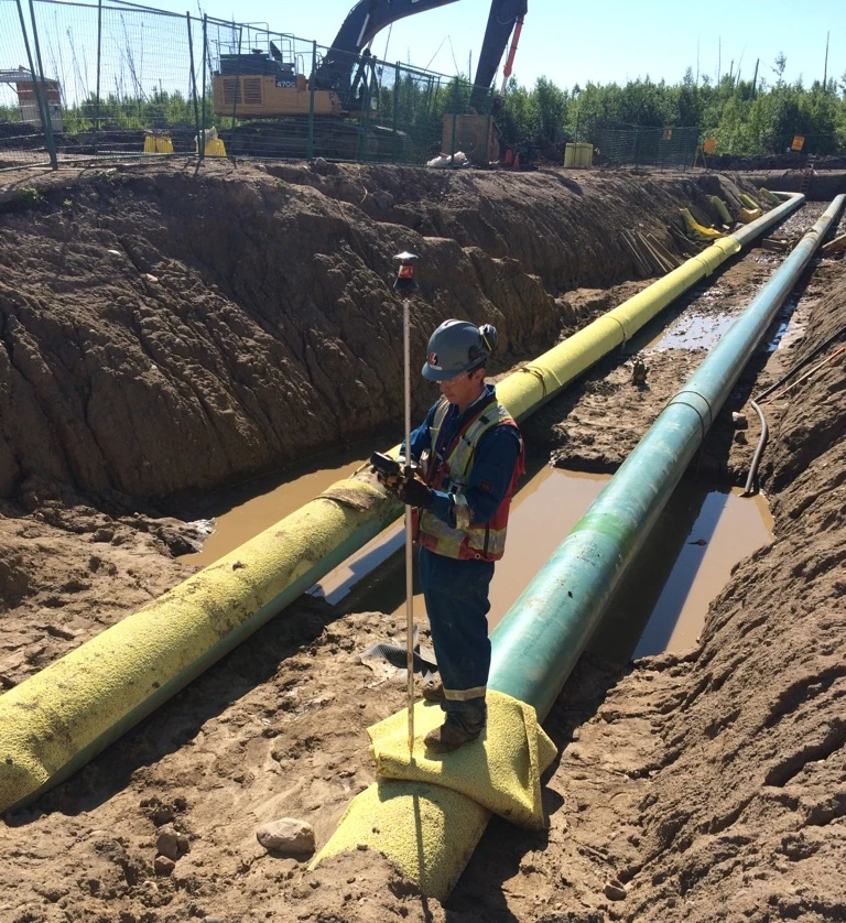 Survey Technician standing on a large pipe in a trench analyzing data
