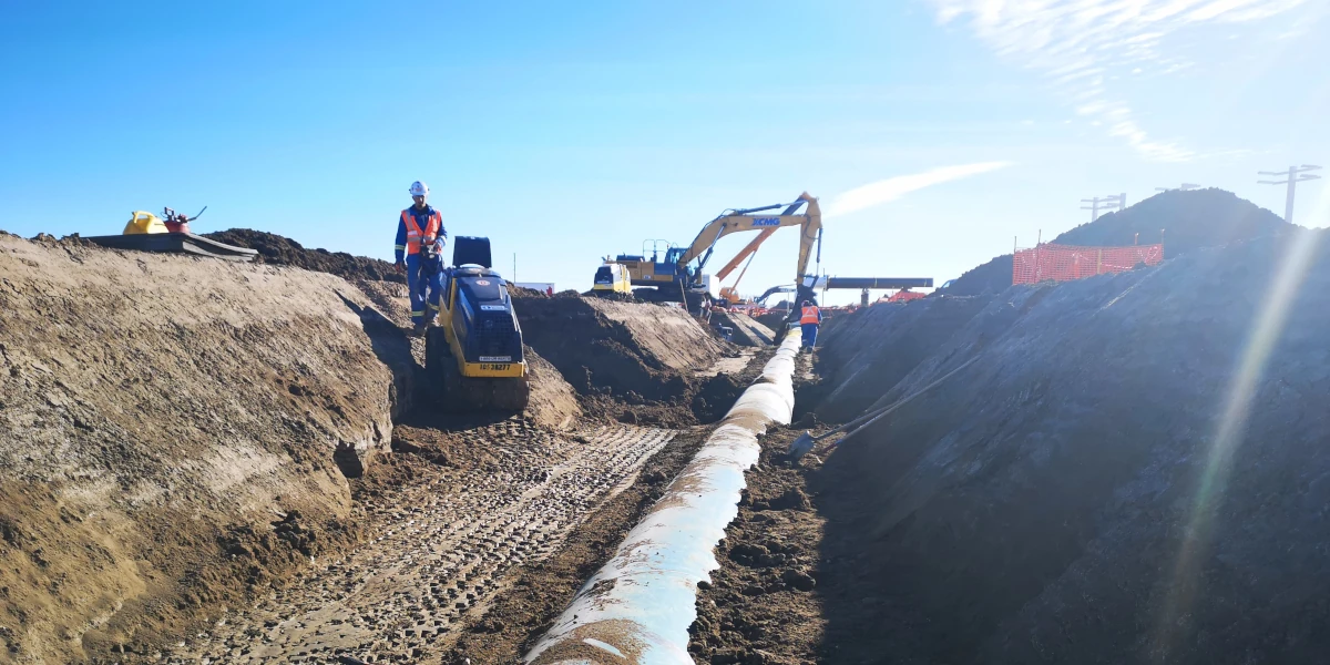 excavator working on pipeline trench, pipe visible on the ground. beautiful sunny day