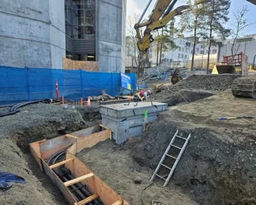 Utility trench at a construction site with a crane placing concrete housing over conduit