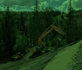 Keltic Geomatics earthworks project on a steep hill among trees, a dump truck is hauling away dirt the excavator is taking off the slope.
